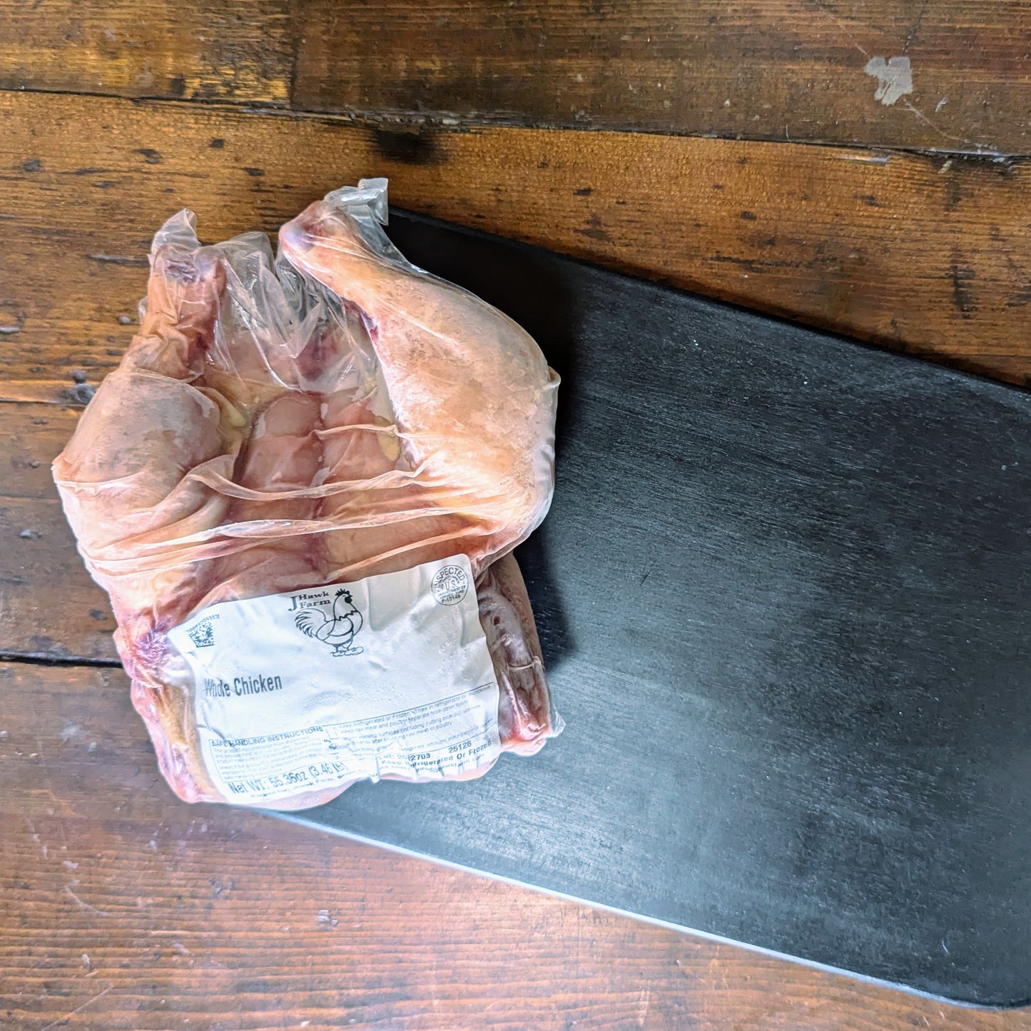 Packaged chicken on a wooden surface with a knife blade.