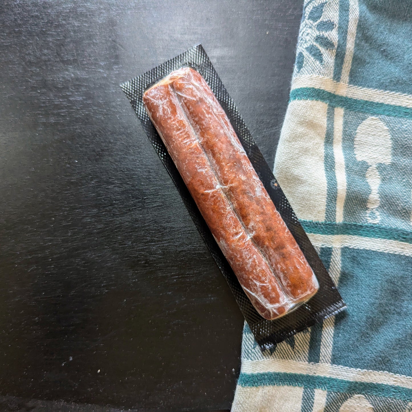 Packaged sausage on a black surface with a patterned cloth underneath
