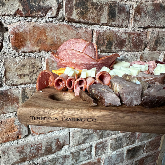 Wooden charcuterie board with meats and cheeses against a brick wall.