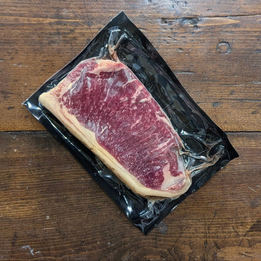 Raw steak on a black plastic wrap against a wooden background