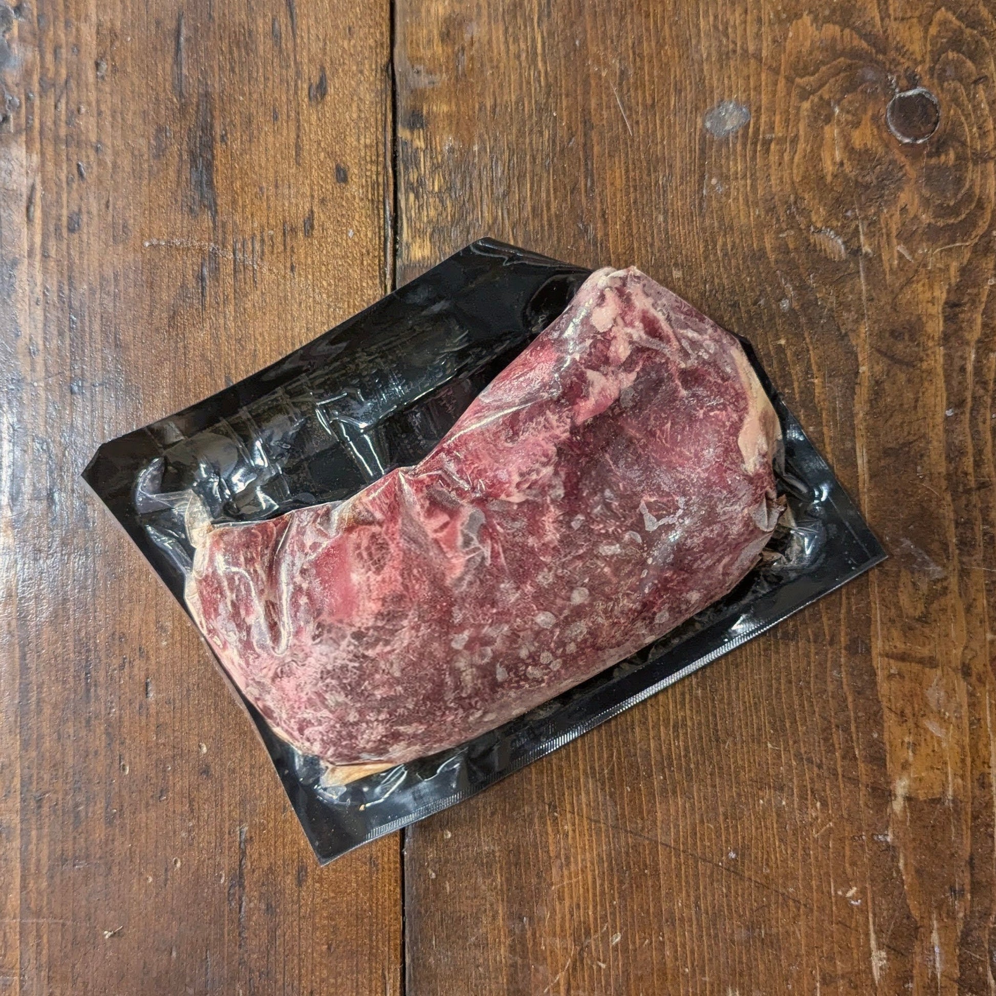 Raw steak in a black plastic packaging on a wooden surface