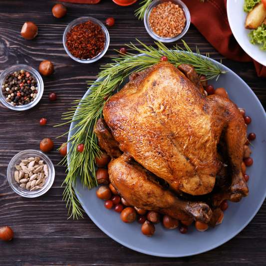 Whole Pasture Raised Turkey on a platter surrounded by herbs, fruit and nuts